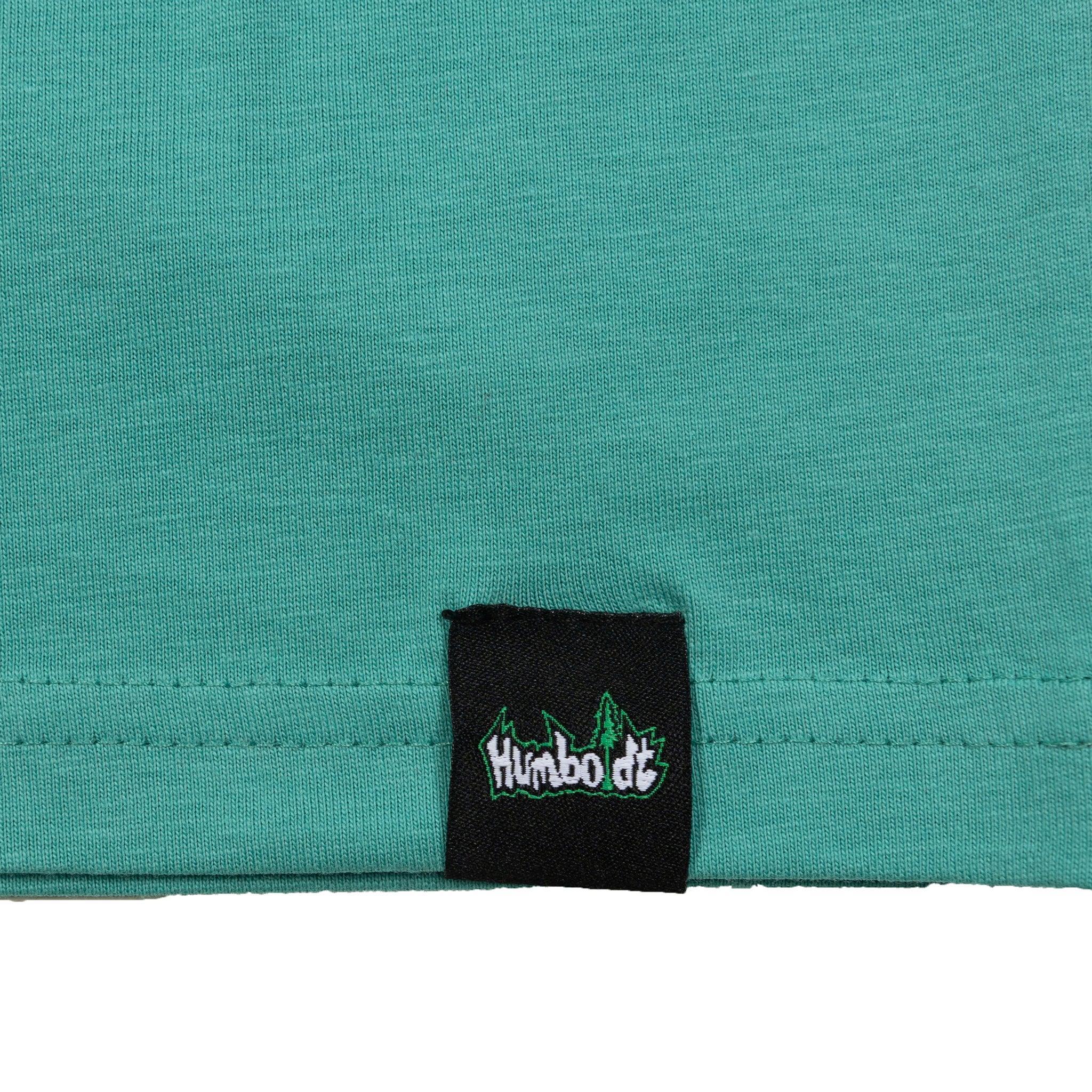 Teal t-shirt hem with black woven label featuring 'Humboldt' logo and tree design, showcasing brand detail.