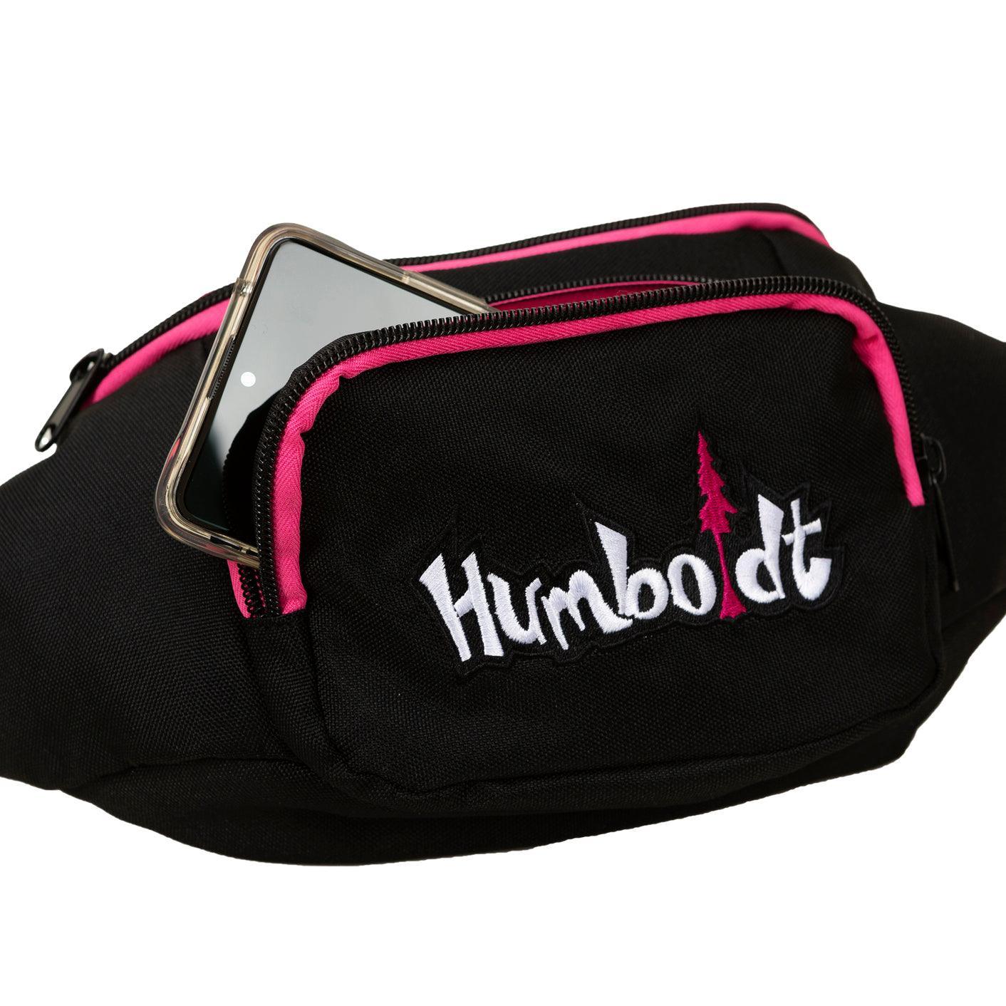 Black fanny pack with pink trim and 'Humboldt' logo, holding smartphone